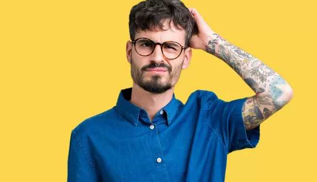 Mann mit ADHS vor gelbem Hintergrund kratzt sich am Kopf
