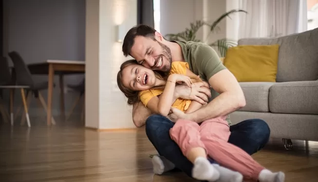 Vater sitzt lachend mit seinem neurodivergenten Kind auf dem Boden – Symbolbild für gelingende Beziehung durch Elterntraining bei ADHS und Autismus